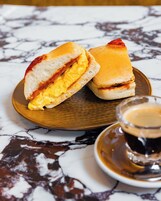 Un sándwich sobre un plato de madera con una taza de café a su lado.