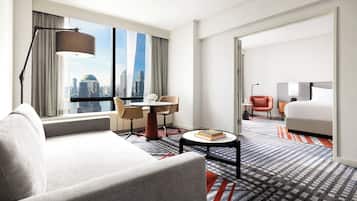 A hotel room with a city view, a sofa, a dining table, and a bed.