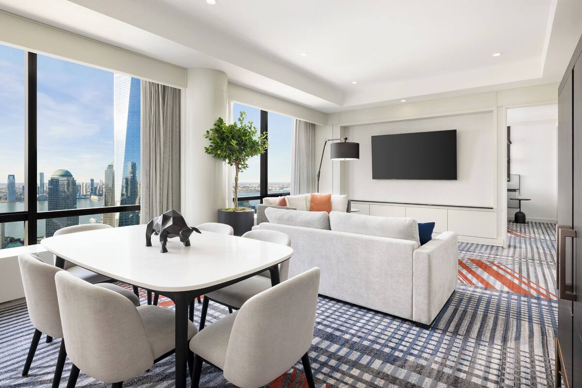 Ein modernes Hotelzimmer mit Essbereich, einer Couch, einem Flachbildfernseher und Blick auf die Stadt.