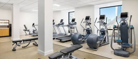 A modern gym with various cardio machines, weight benches, and dumbbells.