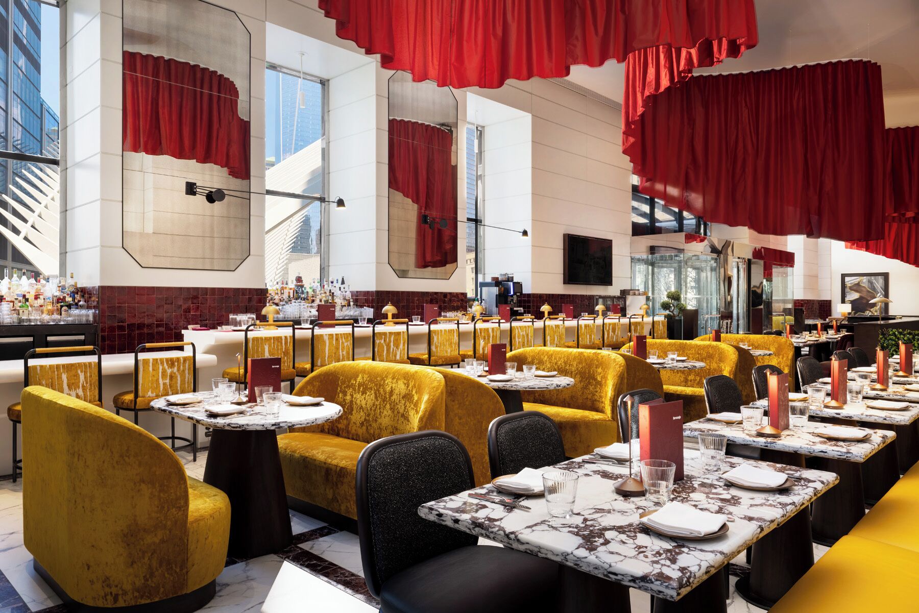 Un restaurante moderno con asientos de terciopelo amarillo, mesas de mármol y cortinas rojas.
