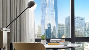Ein modernes Hotelzimmer mit Blick auf einen hohen Wolkenkratzer, ein bequemer Sessel, ein kleiner Tisch mit Büchern und einer Pflanze sowie ein großes Fenster.