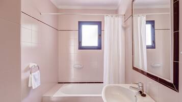 Un baño con bañera, dos lavamanos, un bidé y una ventana con cortina.