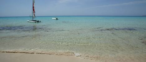 Une plage bordée d’une eau turquoise et limpide, un voilier et un petit bateau à moteur.