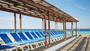 A covered outdoor seating area with blue lounge chairs and a view of the ocean. - Insotel Club Maryland (Formentera)