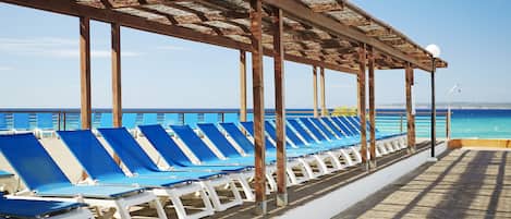 A covered outdoor seating area with blue lounge chairs and a view of the ocean.