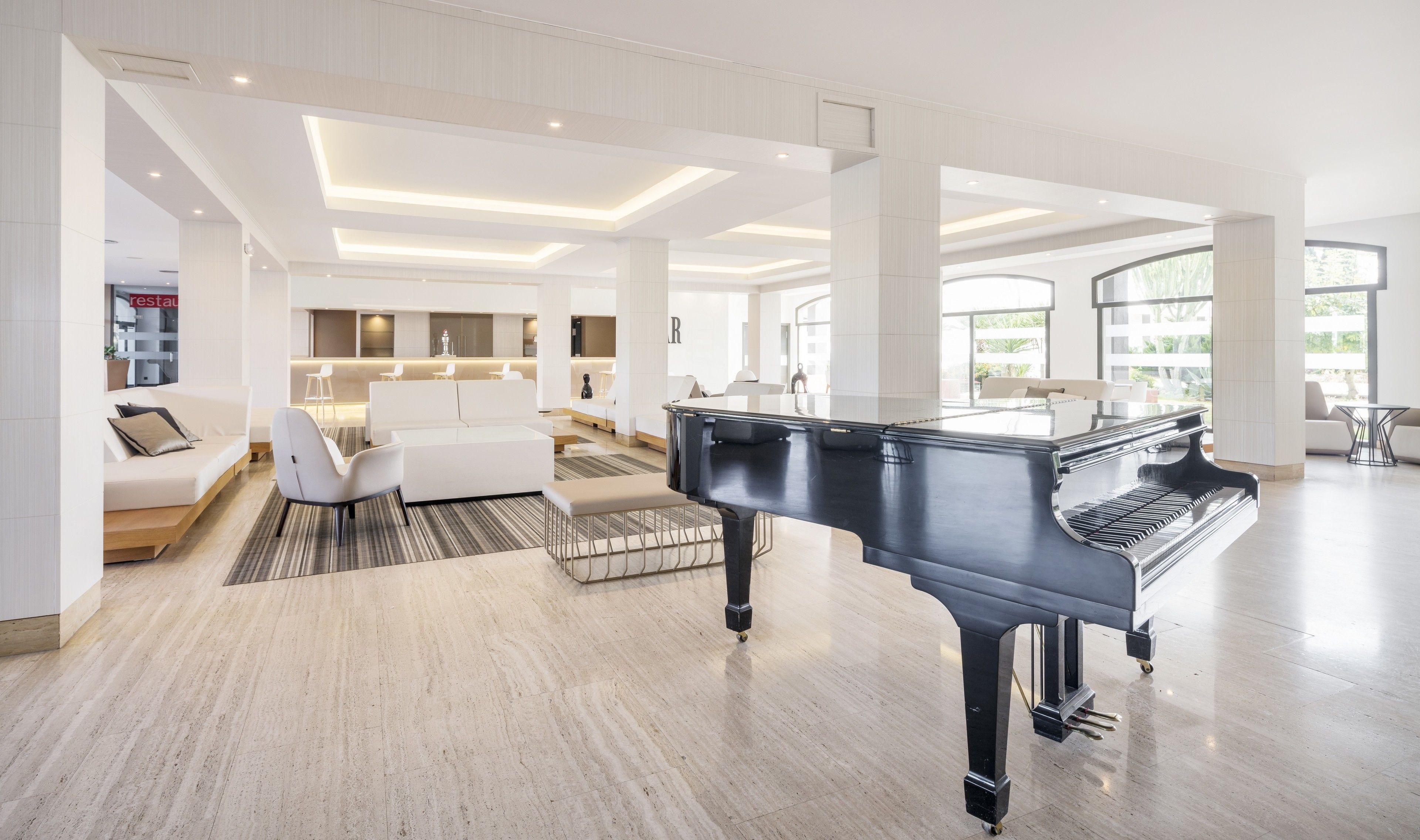 Amplia sala de estar con un piano de cola, un conjunto de sofás modernos y una cocina bien iluminada.