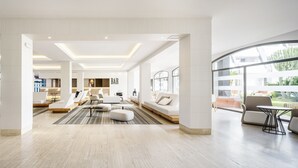 A spacious, modern hotel lobby with a central seating area, a bar, and large windows offering views of the outdoors. - Hotel ILUNION Islantilla (Islantilla)