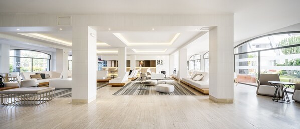 A spacious, modern hotel lobby with a central seating area, a bar, and large windows offering views of the outdoors.