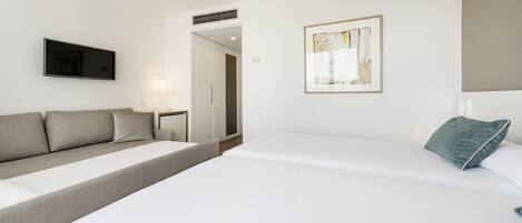 A modern hotel room with a sofa, a bed, a flat-screen TV, a framed abstract painting, and a nightstand with a lamp.