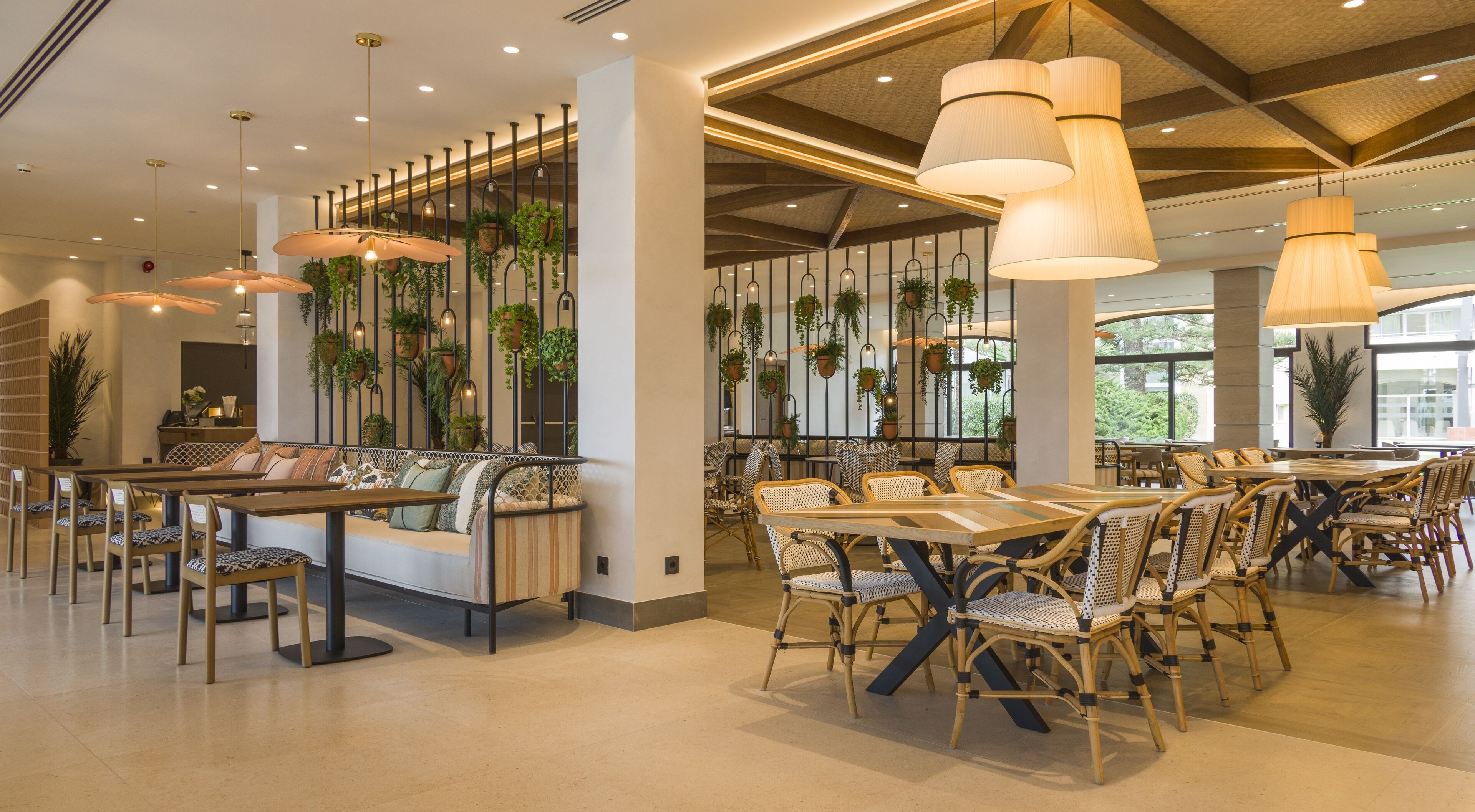 Un restaurante espacioso con techos altos, plantas colgantes y una variedad de opciones de asientos, incluyendo mesas y bancos.