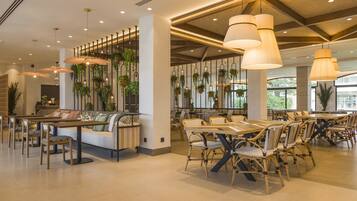 Un restaurante espacioso con techos altos, plantas colgantes y una variedad de opciones de asientos, incluyendo mesas y bancos.