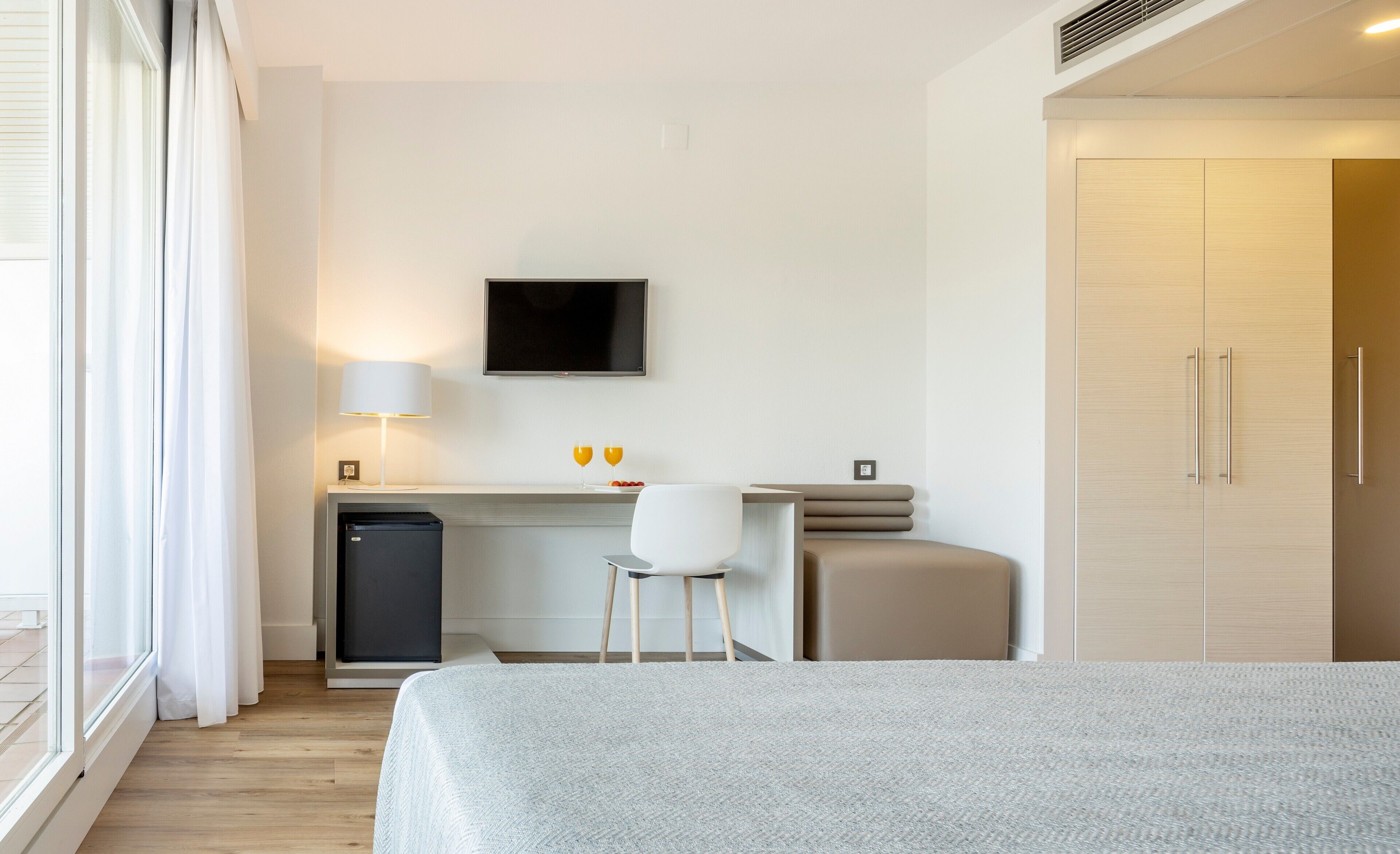 A hotel room with a bed, a desk with a chair, a television, and a wardrobe.