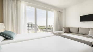 A hotel room with two beds, a sofa, a TV, and large windows with curtains.