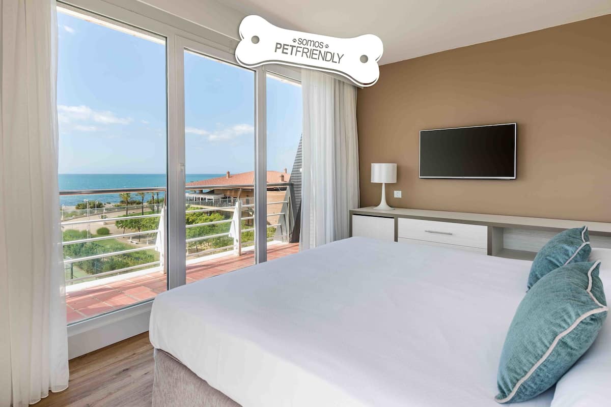 Ein Hotelzimmer mit einem großen Bett, einem an der Wand montierten Fernseher und Meerblick durch große Fenster.