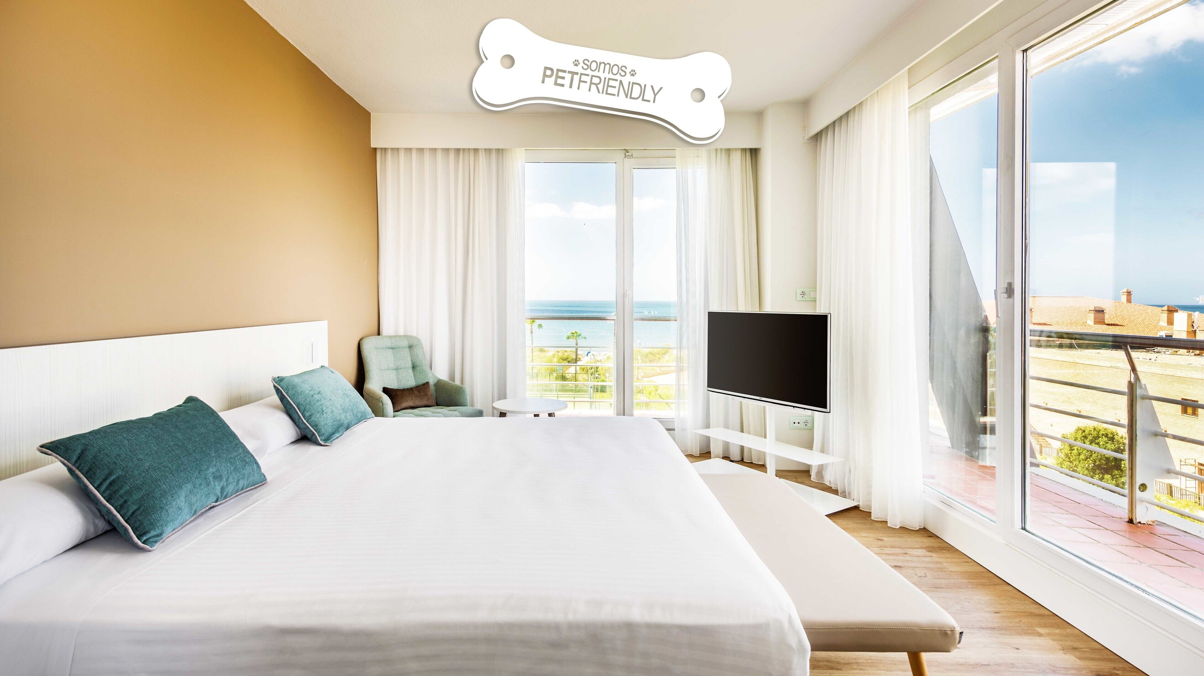 A hotel room with a large bed, a TV, and a balcony with a view of the sea.