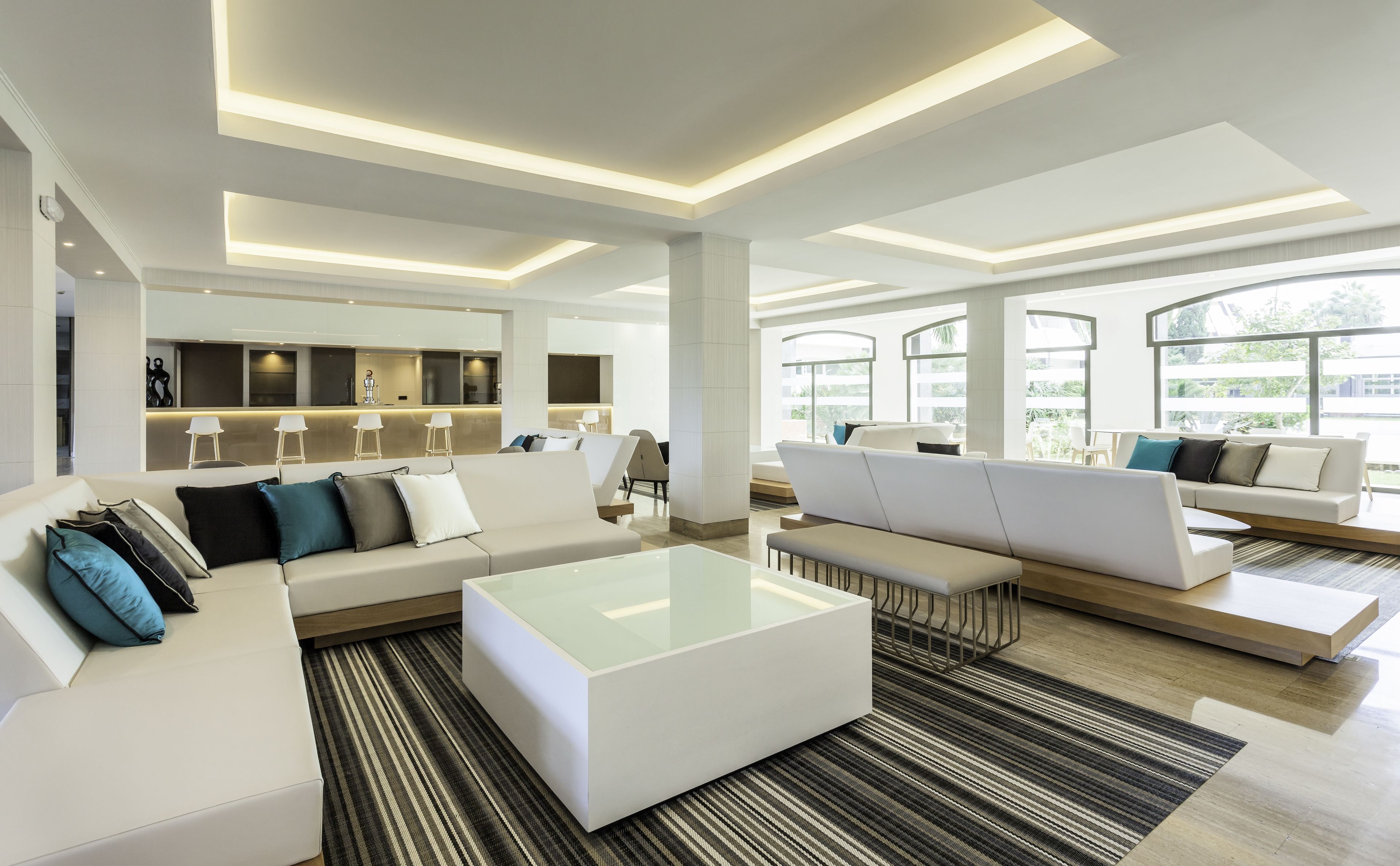 A modern hotel lobby with a central seating area, a bar, and large windows offering a view of the outdoors.