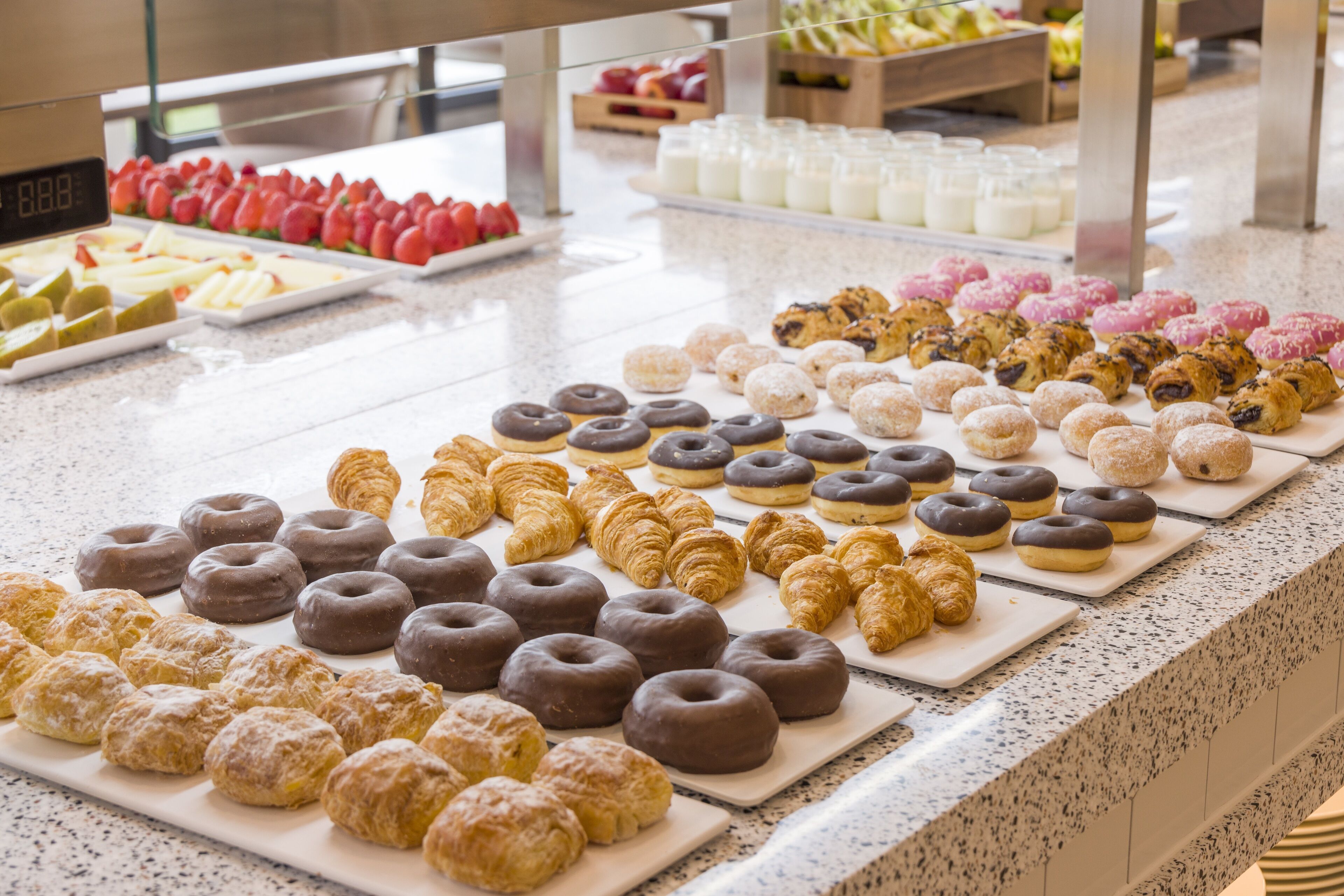 En buffet med forskellige kager og desserter, heriblandt donuts med chokolade og croissanter.