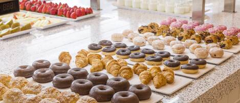 A buffet with various pastries and desserts, including chocolate-covered donuts and croissants.