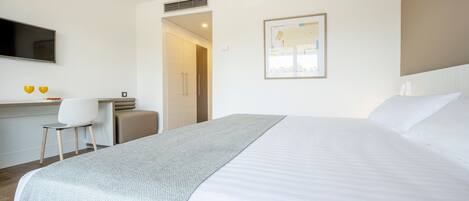 A hotel room with a bed, a desk, a chair, a TV, and a door leading to a bathroom.
