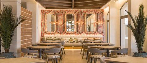 A modern restaurant with a central seating area, multiple tables, and chairs.