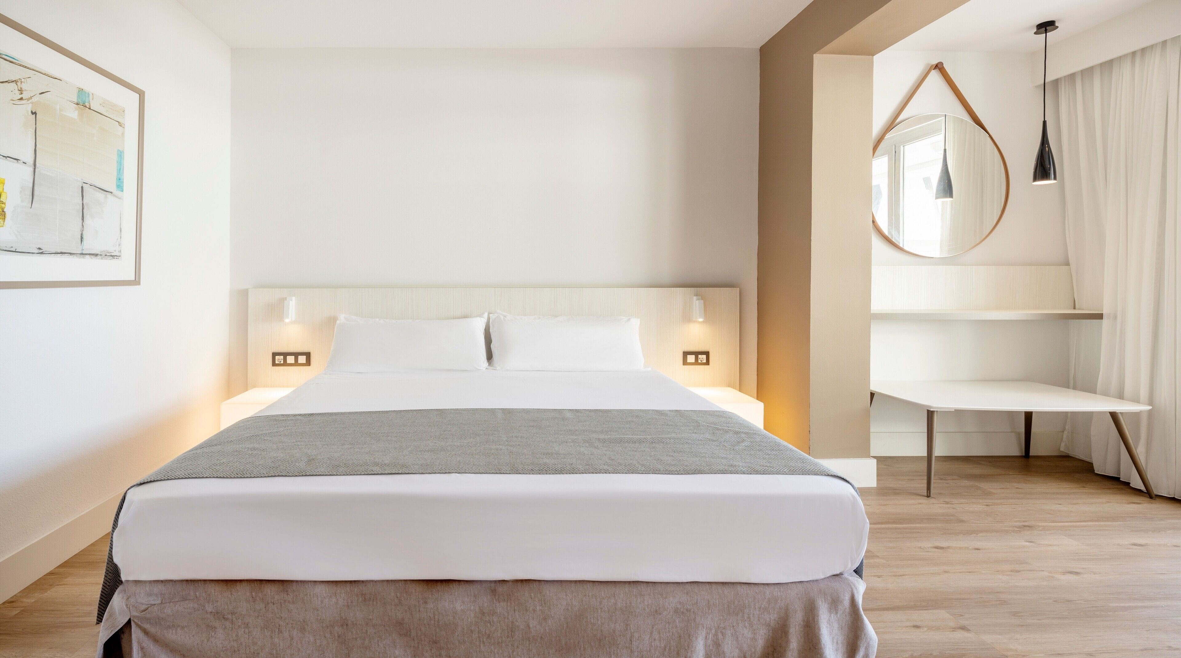 Una habitación de hotel moderna con una cama grande, lámparas de noche, una mesita y un espejo en la pared.