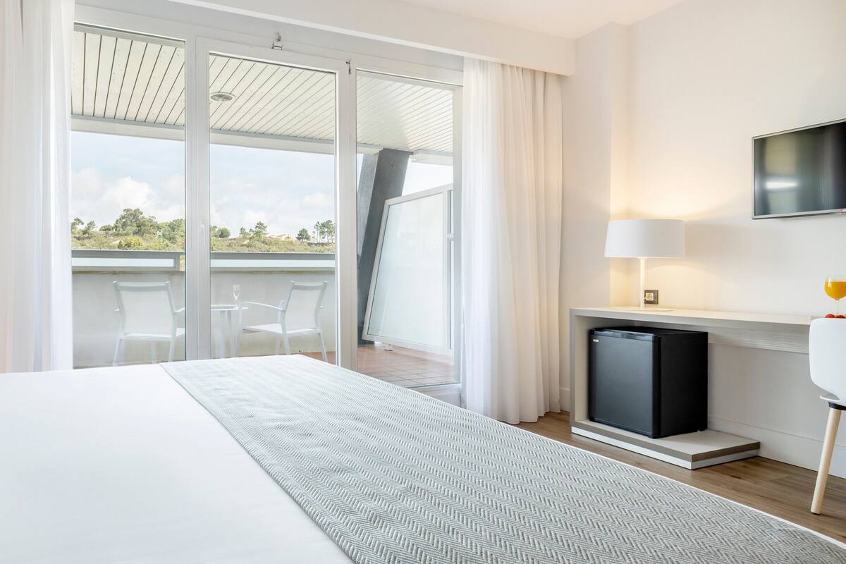 Ein modernes Hotelzimmer mit einem großen Bett, einem Flachbildfernseher, einer kleinen Sitzecke und einem Balkon mit Landschaftsblick.