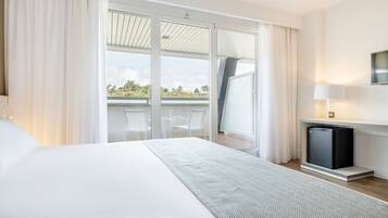 Een moderne hotelkamer met een groot bed, een flatscreen-tv, een zithoekje en een balkon met uitzicht op het landschap.