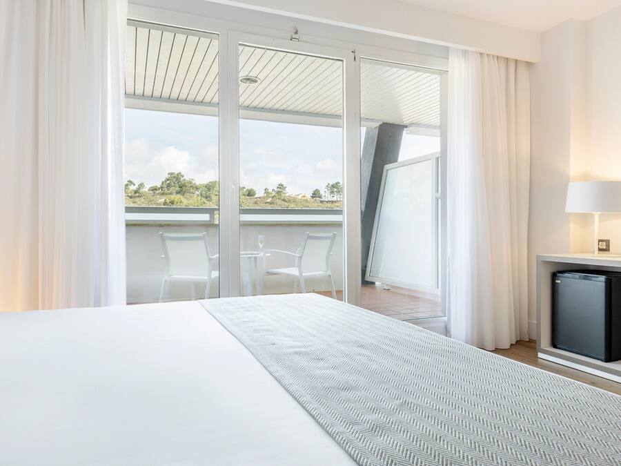 Een moderne hotelkamer met een groot bed, een flatscreen-tv, een zithoekje en een balkon met uitzicht op het landschap.