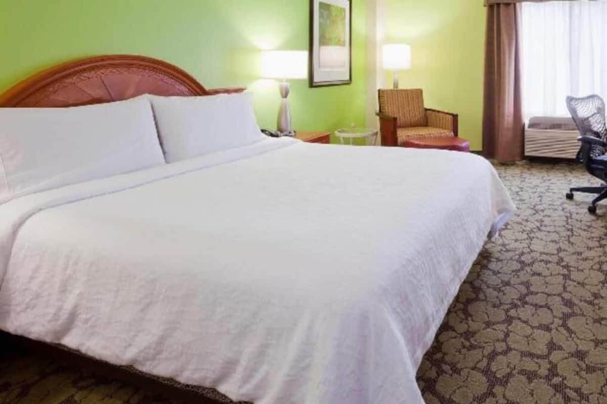 A hotel room with a large bed, a chair, a desk, and a lamp.