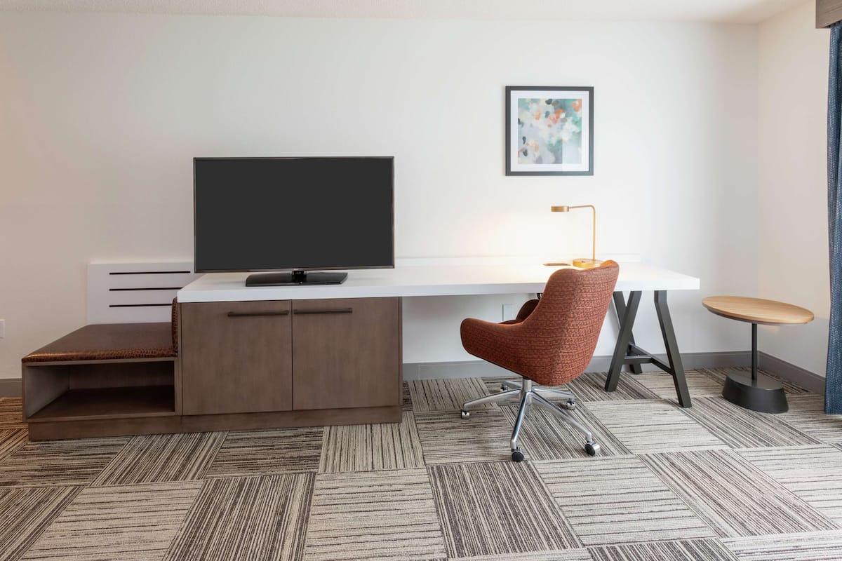 A modern office space with a white desk, a television, a brown chair, and a small round table.