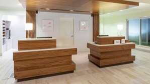 A hotel reception area with wooden reception desks, a white door, and framed artwork on the walls. - Hilton Garden Inn Minneapolis/Bloomington (Bloomington)