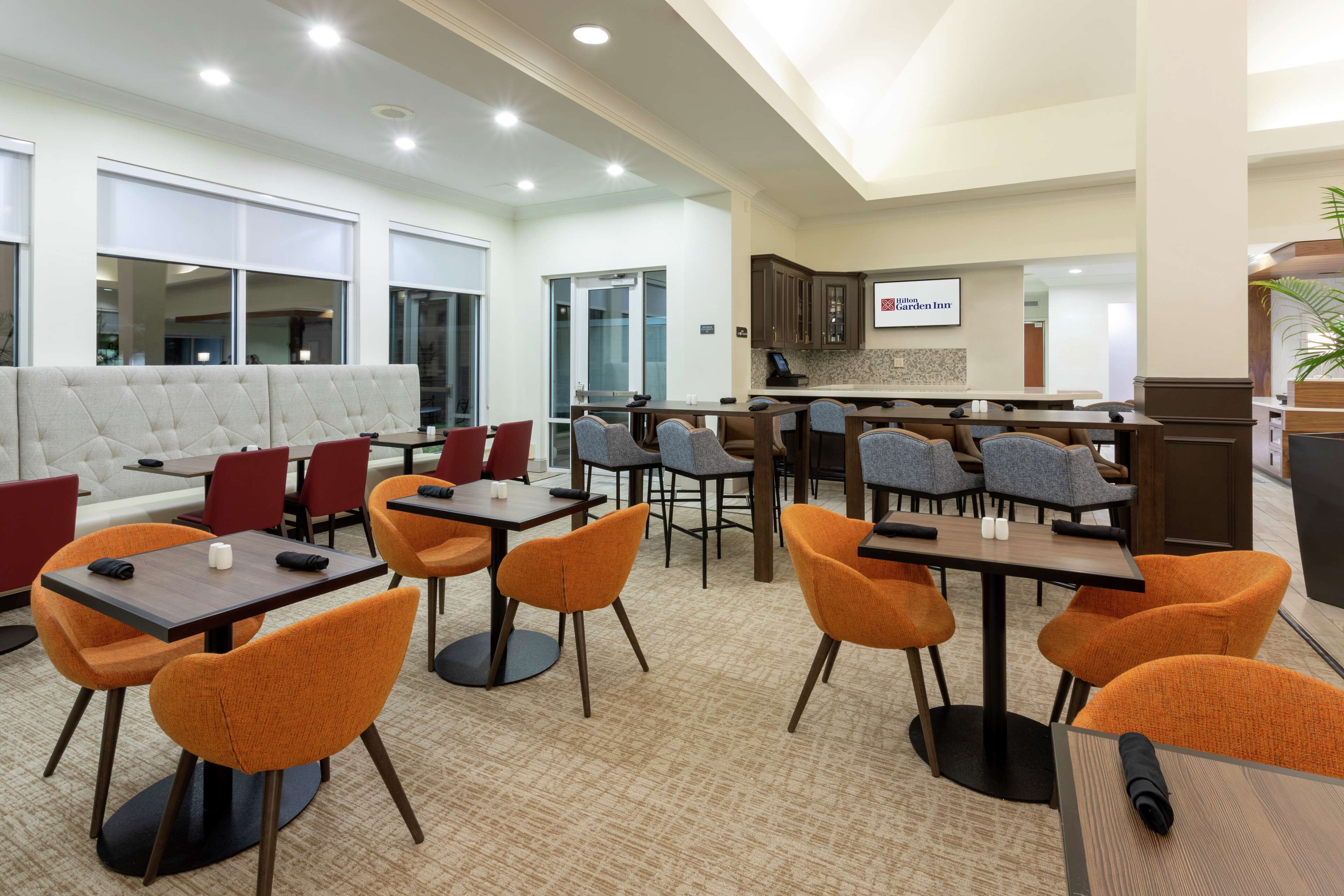 A modern hotel lobby with a seating area, a bar, and a kitchen visible in the background.