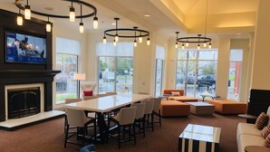 A spacious living area with a fireplace, a large TV screen, and modern lighting fixtures. - Hilton Garden Inn Minneapolis/Bloomington (Bloomington)