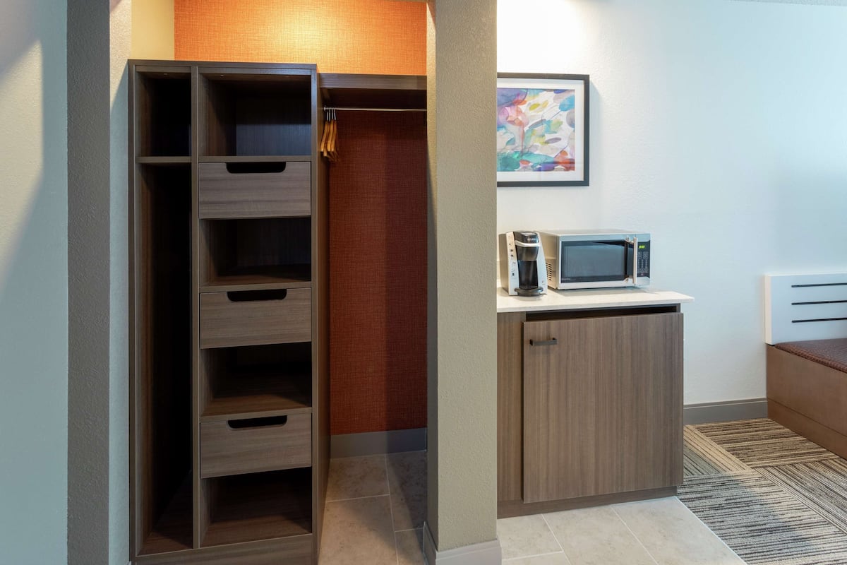 A compact kitchenette with a microwave, a small cabinet, and a wooden cabinet.
