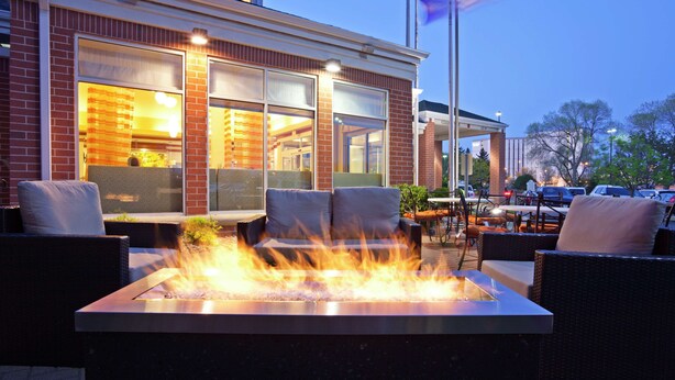 An outdoor seating area with a fire feature, wicker furniture, and a view of the building's interior. - Hilton Garden Inn Minneapolis/Bloomington (Bloomington)