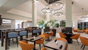 A hotel lobby with multiple seating areas, including tables and chairs, and a large screen displaying the hotel name. - Hilton Garden Inn Minneapolis/Bloomington (Bloomington)