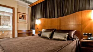 Habitación de hotel con una cama grande, cabecera de madera, mesita de noche con lámpara y un espejo.