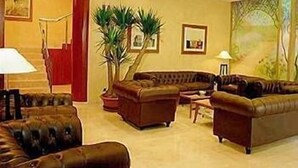 Amplia sala de estar con un conjunto de sofá de cuero marrón, una mesa de centro y una planta grande en maceta. Se observa una escalera con una pared de acento roja y un cuadro en la pared.