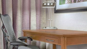 A wooden desk with a modern desk lamp, a chair, and a framed picture on the wall.