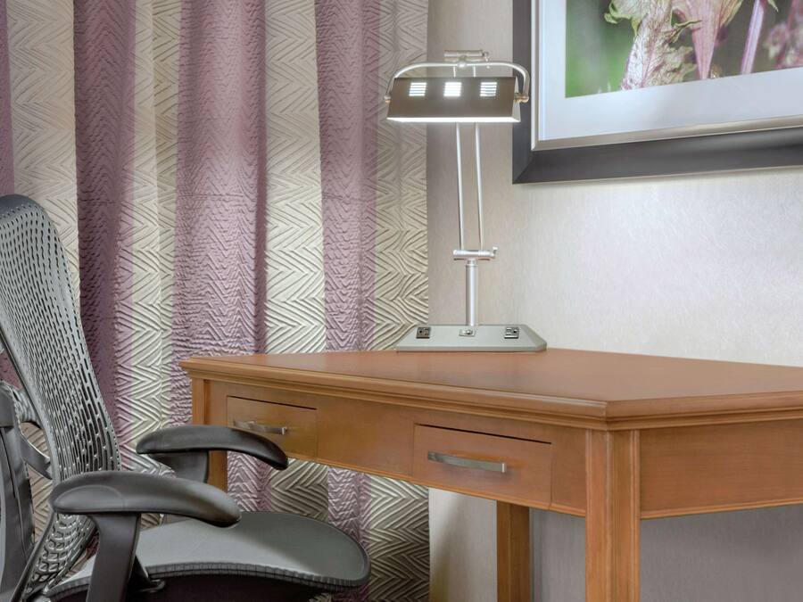 A wooden desk with a modern desk lamp, a chair, and a framed picture on the wall.
