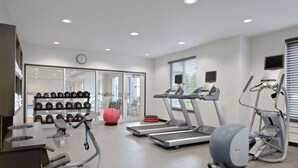 A modern gym with treadmills, an elliptical, and a rowing machine. There are dumbbells and a red exercise ball.