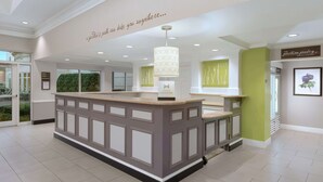 A hotel reception area with a central counter, a sign reading "The Pavilion Pantry," and a wall with a quote.