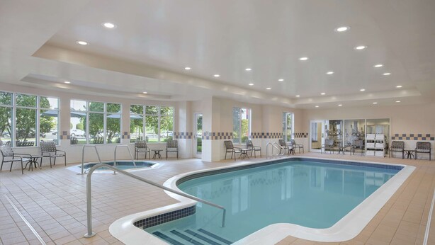 An indoor swimming pool with tiled flooring, metal railings, and multiple seating areas with chairs and tables.