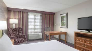 Een hotelkamer met een groot bed, een bureau, een stoel, een televisie en een raam met gordijnen.