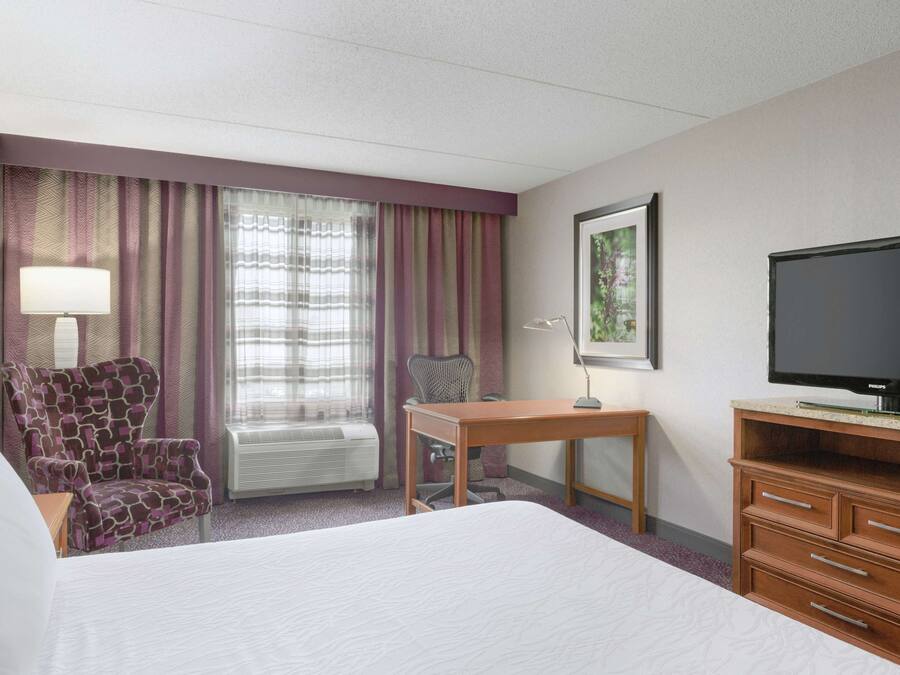 Een hotelkamer met een groot bed, een bureau, een stoel, een televisie en een raam met gordijnen.