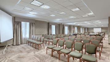 A conference room with rows of chairs, a projector screen, and a carpet with a floral pattern.
