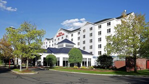 A large, multi-story hotel with a prominent 'Hilton Garden Inn' sign, surrounded by well-maintained landscaping and a clear sky.