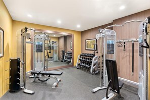 Un gimnasio con equipos de ejercicio variados, una banca y un estante con mancuernas.