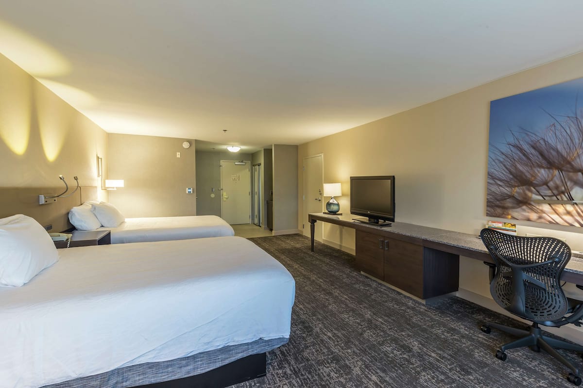 A hotel room with two beds, a desk with a chair, a television, and a painting on the wall.